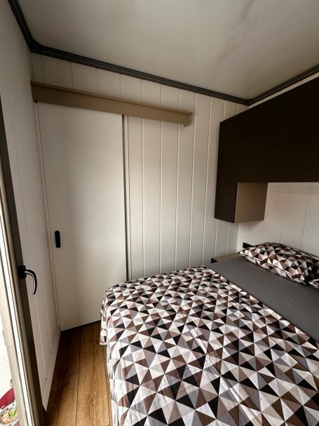 Dormitorio luminoso con puerta corredera Habitación pequeña con una cama y una pared con un armario blanco. Diseño moderno.