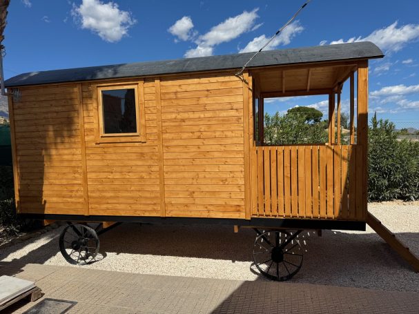 Vista lateral del Circus Wagon 5 m Casa de madera sobre ruedas, con ventana y verandita, ubicada al aire libre.