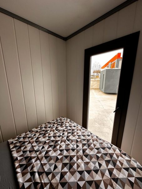 Habitación con cama y puerta abierta hacia el exterior, mostrando un entorno rural.