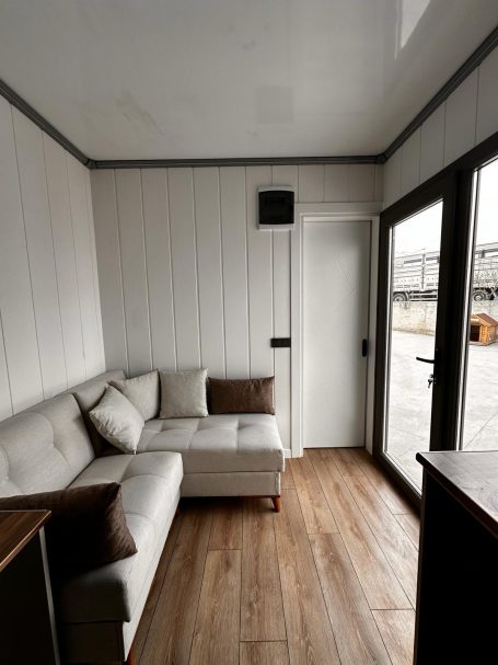 Salón con sofá en L y acceso exterior Salón moderno con sofá claro, mesa, y ventanales que ofrecen luz natural.