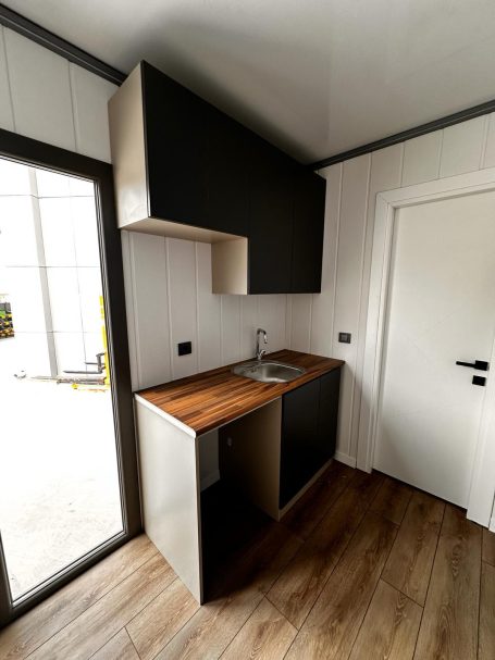 Cocina compacta totalmente equipada Cocina pequeña con armarios oscuros y encimera de madera, puerta blanca a un lado.