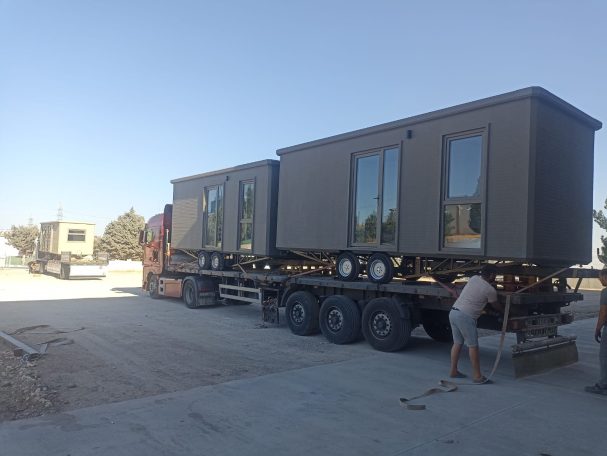 Transporte de unidades móviles listas para usar Remolque de casas modulares en un terreno, con un obrero trabajando cerca.